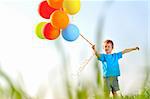 Young boy playing with a bunch of balloons outside, shot through grass in the field