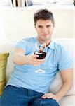 Charming young man sitting on a sofa holding wineglass in the living room