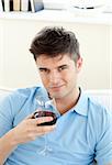 Handsome young man sitting on a sofa holding wineglass in the living room