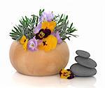 Lavender herb leaf sprigs and yellow viola flowers in a beech wood mortar with pestle with grey spa stones, isolated over white background. Herbs for skincare.