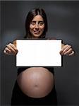 Pregnant woman holding a white card over a gray background.