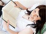 Bright brunette teenager holding a book smiling at the camera in the living room