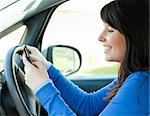 Brunette young woman sending a message with her mobile phone sitting in her car