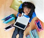 Cheerful afro-american teenager using a laptop sitting between shopping bags on the floor in the living room