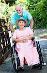 Senior man pushing his disabled wife through the park in a wheelchair.