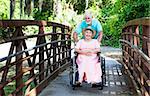 Senior man pushes his disabled wife through the park in a wheelchair.