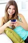 Smiling young woman texting sitting on the sofa in the living room