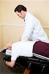 Chiropractor adjusts a senior man's spine on his examining table.