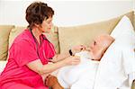 Home nurse helps elderly patient drink a glass of orange juice.