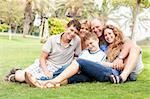 Family of five relaxing on sunny day in the park and smiling at camera