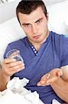 Dejected young man holding pills and water sitting on the sofa looking at the camera