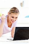 Delighted young woman looking at her laptop lying on the floor in the living-room