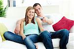 Positive young couple sitting on the sofa watching tv in the living room