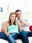 Glowing young couple sitting on the sofa watching tv in the living room