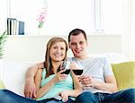 Young embracing  couple sitting on the sofa drinking wine at home