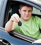 Happy young male driver sitting in blue car and holding his car key