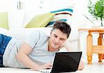Positive young man using his laptop lying on the floor at home