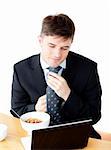 Attractive young businessman making his tie looking at his laptop at the breakfast table