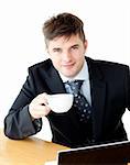 Charming young businessman holding a cup smiling at the camera sitting against white background