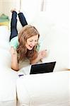 Enthusiastic caucasian woman looking at her laptop on the sofa at home