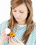 Concentrated female patient looking at her pills against white background