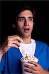 admired young man, with popcorn watching a film, on black background. Studio shot