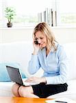 Glowing businesswoman using her phone and laptop in her living-room at home