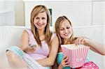 Relaxed female friends eating popcorn watching tv at home