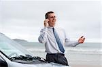 Smiling businessman talking on cell phone by his car on a beach