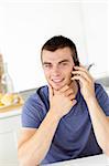 Handsome young man talkng on phone and smiling at the camera at home