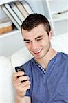 Charming young man sending a text and smiling in the living-room at home