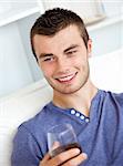 Handsome young man holding a glass of wine sitting on a sofa in the living-room at home