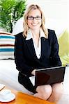 Merry businesswoman with glasses using her laptop on a sofa at home