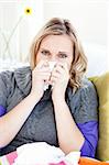 Sick woman using a tissue sitting on a sofa at home