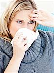 Dejected woman using a tissue sitting on a sofa at home