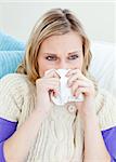 sick woman using a tissue sitting on a sofa at home