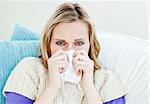 Diseased woman using a tissue sitting on a sofa at home
