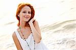 Beautiful young red-haired on the beach at sunset. Photo with counter-light on background.