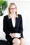 confident business woman with glasses drinking coffee at home sitting in the sofa