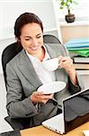 Smiling businesswoman holding a coffee while using a laptop at work in her office