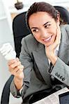 Young businesswoman holding a light bulb sitting in her office at her desk