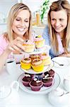 Positive young women eating cakes in the kitchen at home