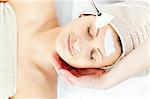 Pretty relaxed woman receiving white cream on her face in a spa center