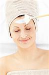 Smiling relaxed woman receiving white cream on her face in a spa center