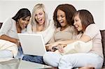 A group of four interracial beautiful young women having fun looking at something surprising and funny on their laptop computer and laughing