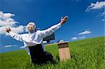 Business concept shot showing an older male executive arms raised using a computer in a green field with a blue sky complete with fluffy white clouds. Shot on location not in a studio.