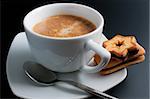 White porcelain cup of freshly brewed coffee close-up arranged with two  sandwich-biscuits spoon and plate on dark background