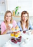 Portrait of two female friends eating pastries and drinking coffee in the kitchen at home