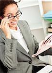 Smiling businesswoman with glasses and a newspaper sitting at her desk in her office