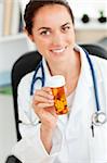 Delighted female doctor holding pills into the camera in her office sitting at her desk